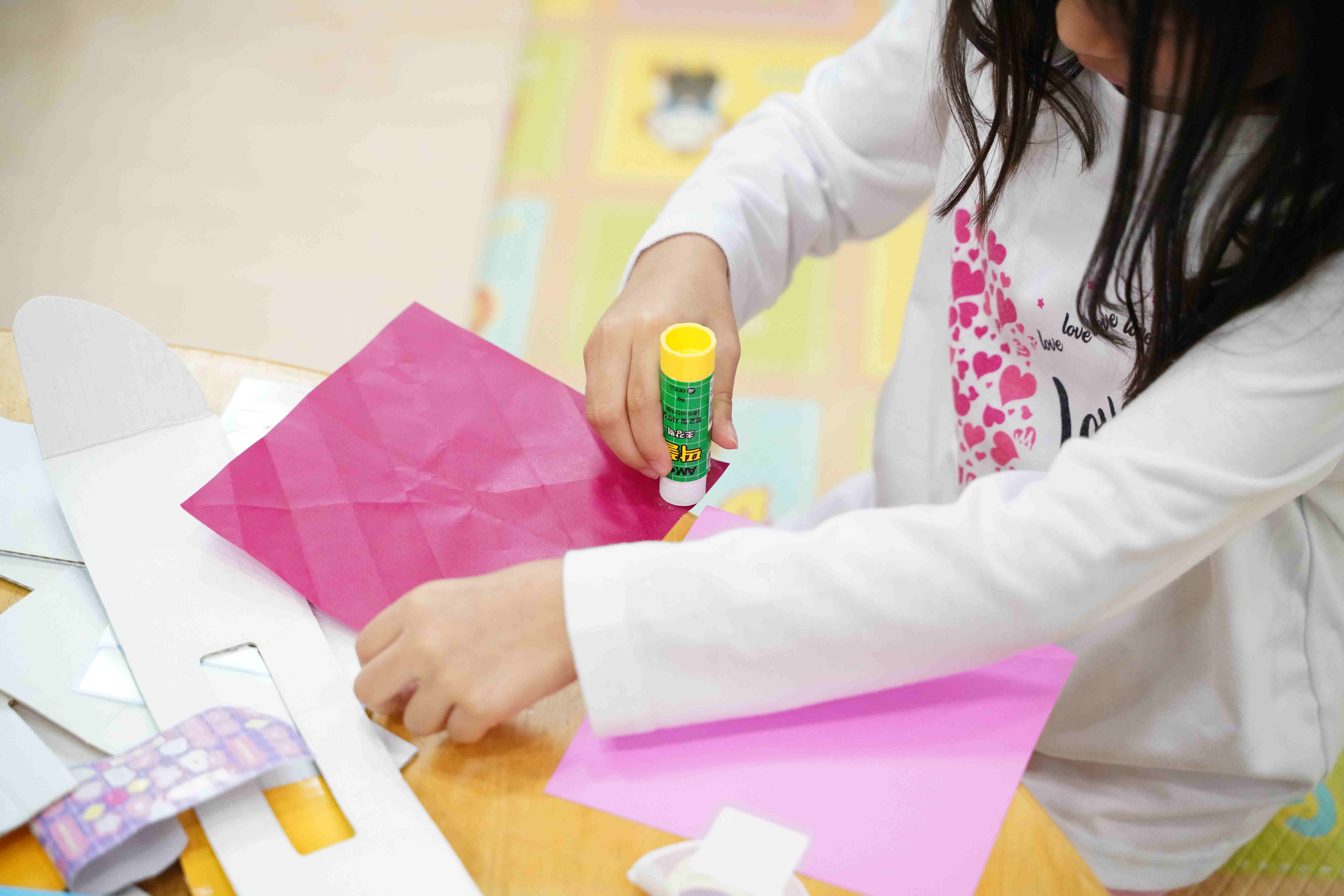 아이가 분홍색 종이에 풀을 바르며 미술 활동을 하는 모습