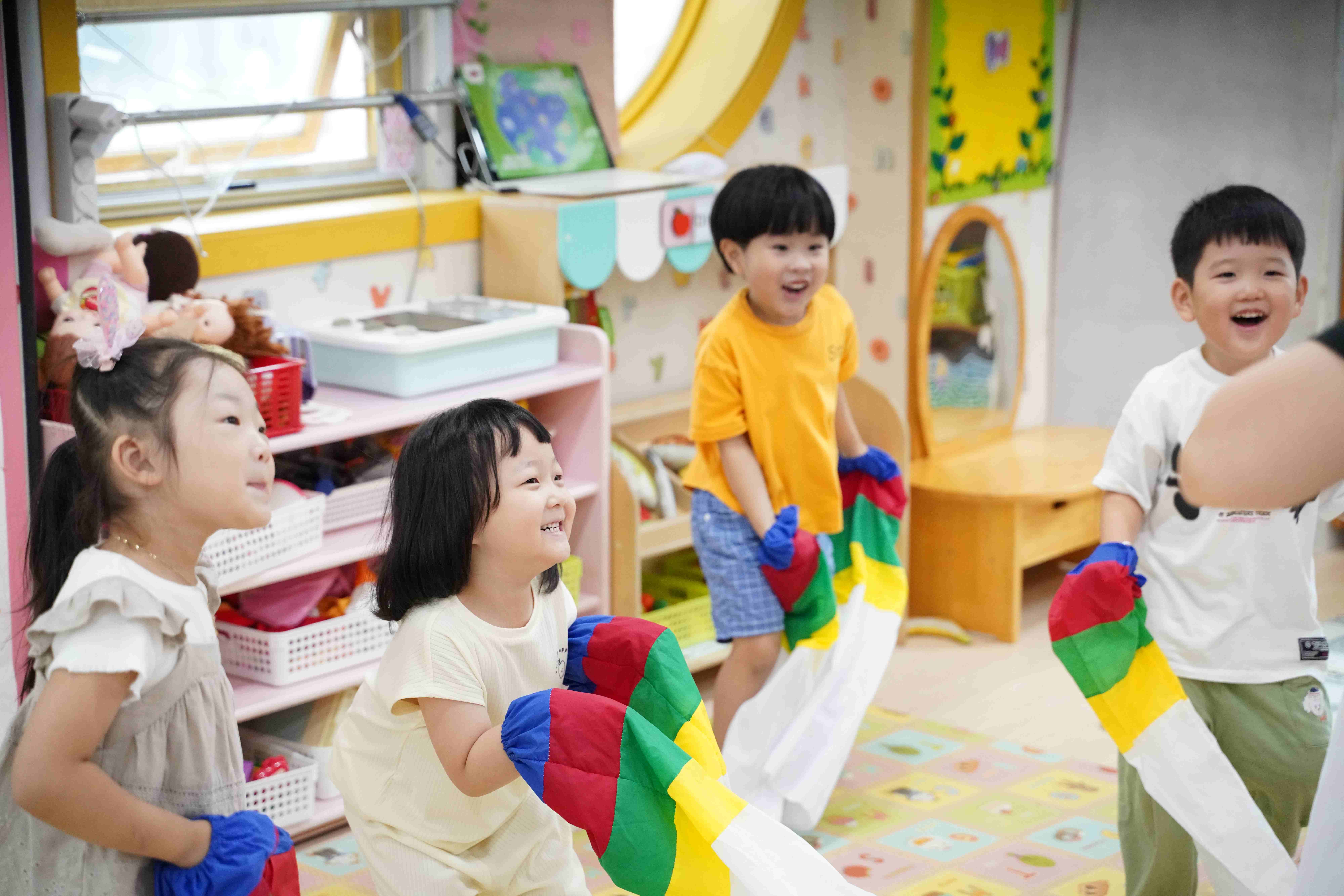 아이들이 교실에서 색색의 낙하산을 들고 즐겁게 활동하는 모습